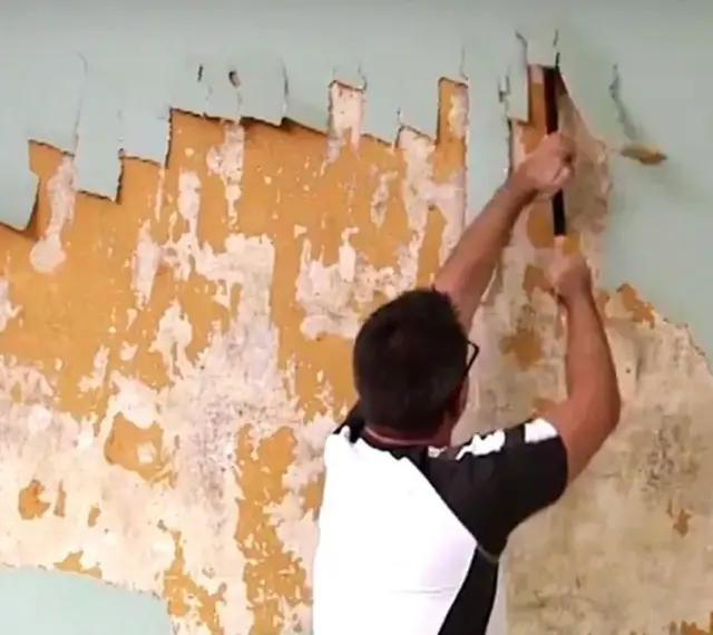 Man scraping old wallpaper off a wall.