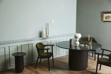 Ett runt matbord med mörka stolar skapar en inbjudande atmosfär. Utrymme runt matbordet ger plats för samtal och gemenskap.